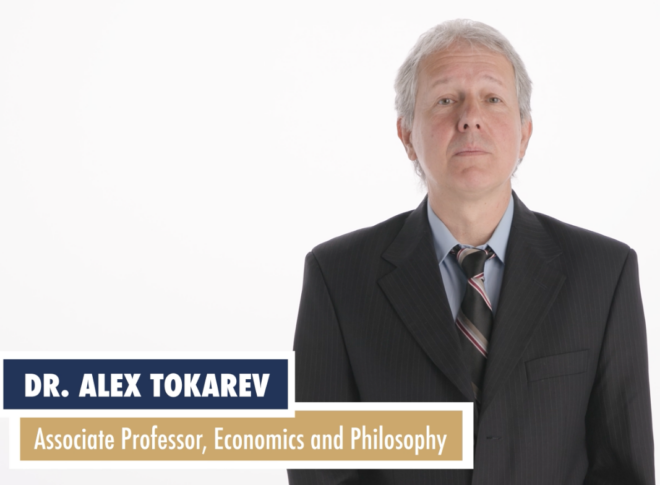 A man in a suit with a striped tie stands against a white background. The text reads: "Dr. Alex Tokarev, Associate Professor, Economics and Philosophy, specializing in free enterprise.